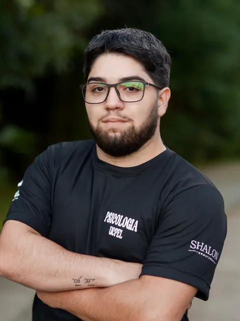 Bruno de Souza Gonçalves, de óculos e camiseta preta, com os braços cruzados, ao ar livre.